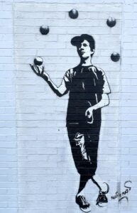 Street art stencil of boy in cap juggling five balls.